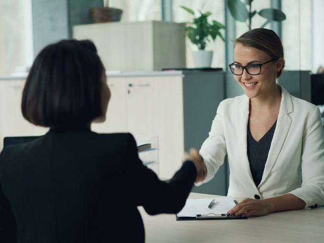 A recruiter shaking hands with a candidate across a desk after an interview